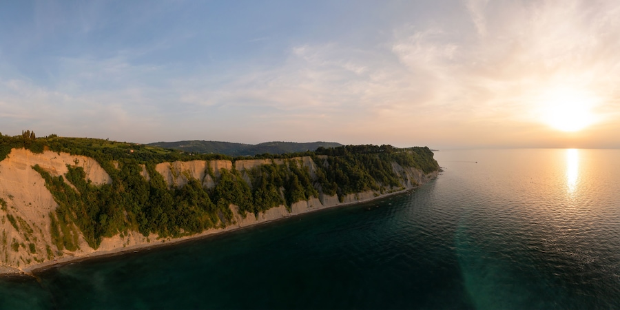 Eine Küstenlandschaft mit Klippen, einem Strand und einem ruhigen Meer bei Sonnenuntergang.