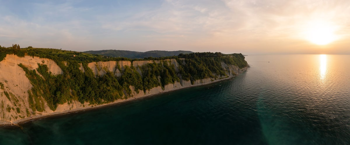 A coastal landscape with cliffs, a beach, and a calm sea during sunset.