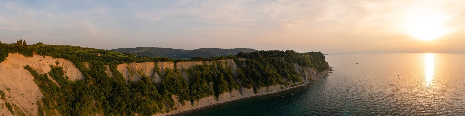 A coastal landscape with cliffs, a beach, and a calm sea during sunset.