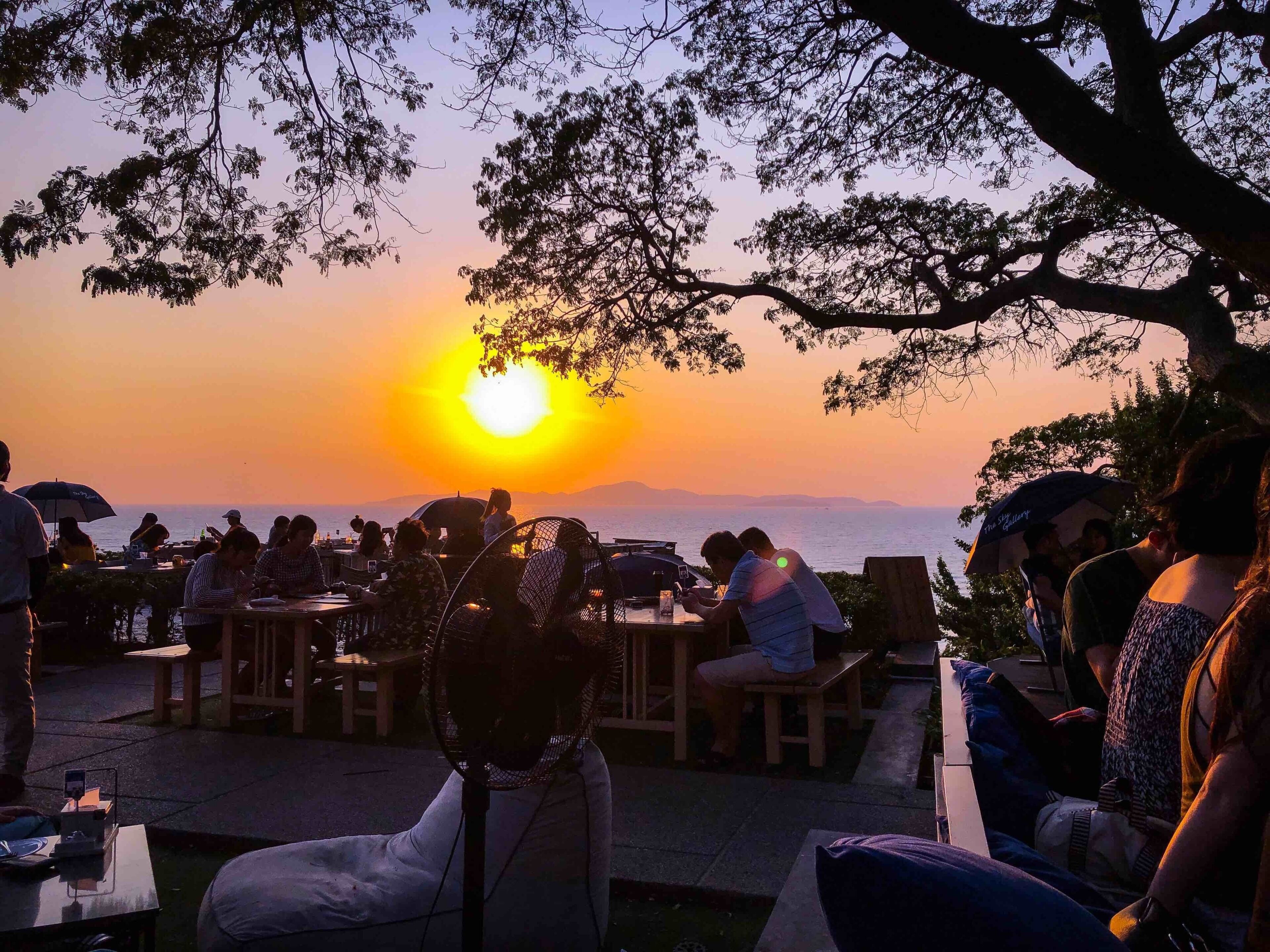 A sunset over a body of water with people dining at tables.