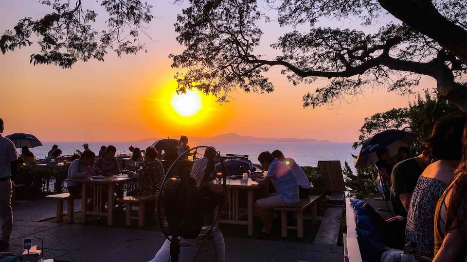 A sunset over a body of water with people dining at tables.