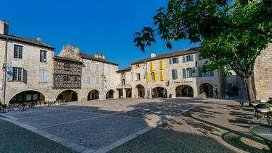 A historic stone courtyard with arches, a café, and a building labeled "Office de Tourisme".