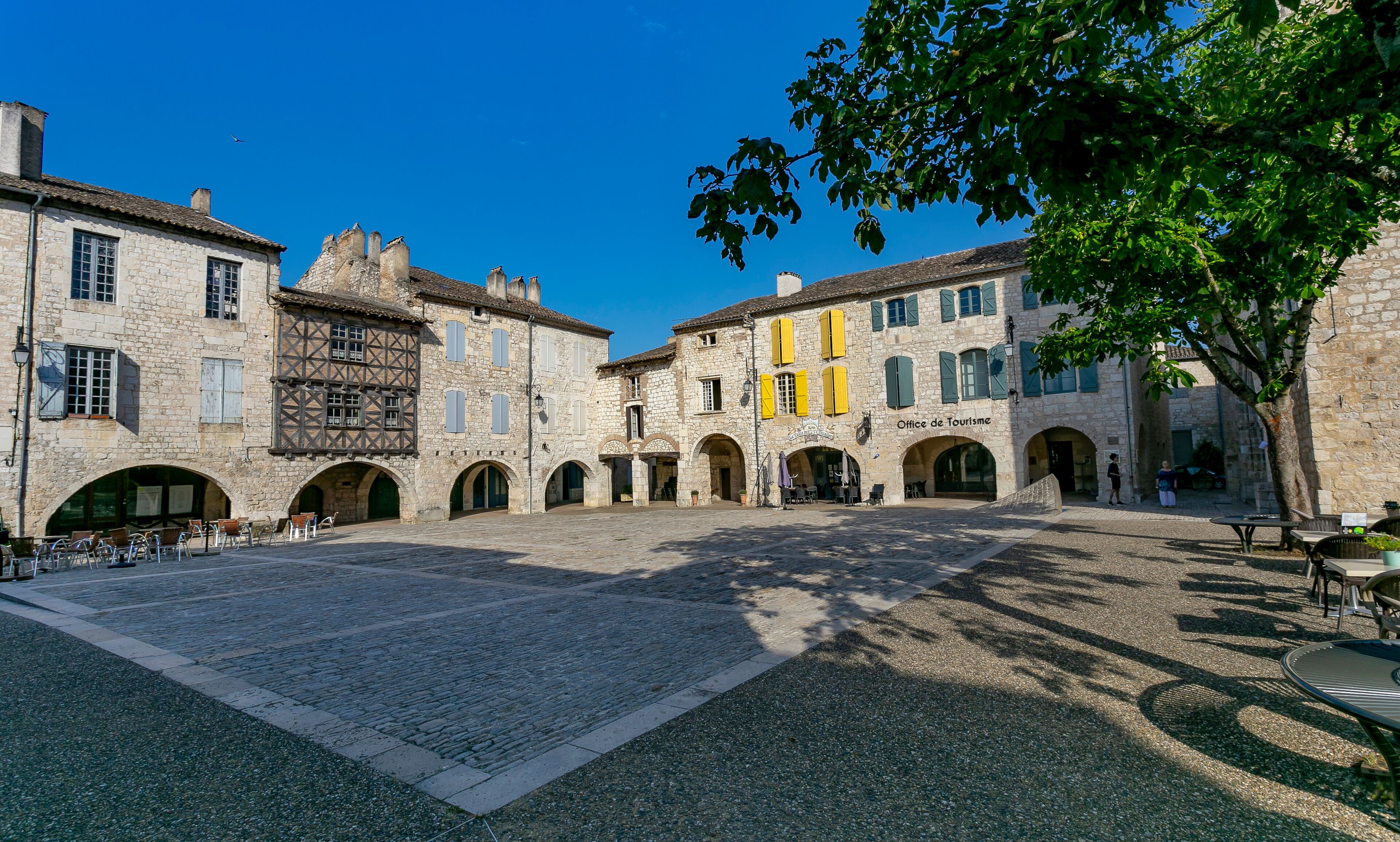 A historic stone courtyard with arches, a café, and a building labeled "Office de Tourisme".