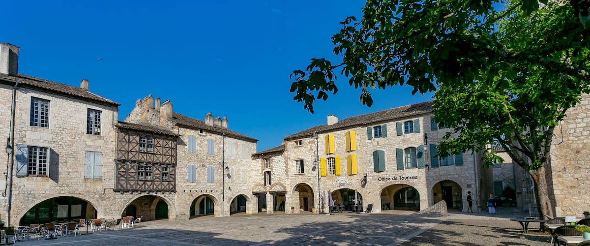 A historic stone courtyard with arches, a café, and a building labeled "Office de Tourisme".