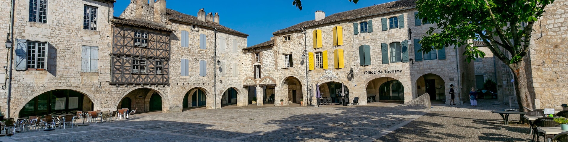 A historic stone courtyard with arches, a café, and a building labeled "Office de Tourisme".