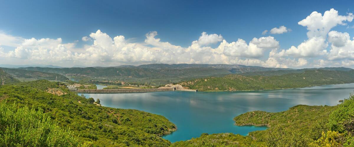 A lake surrounded by green hills and a dam.