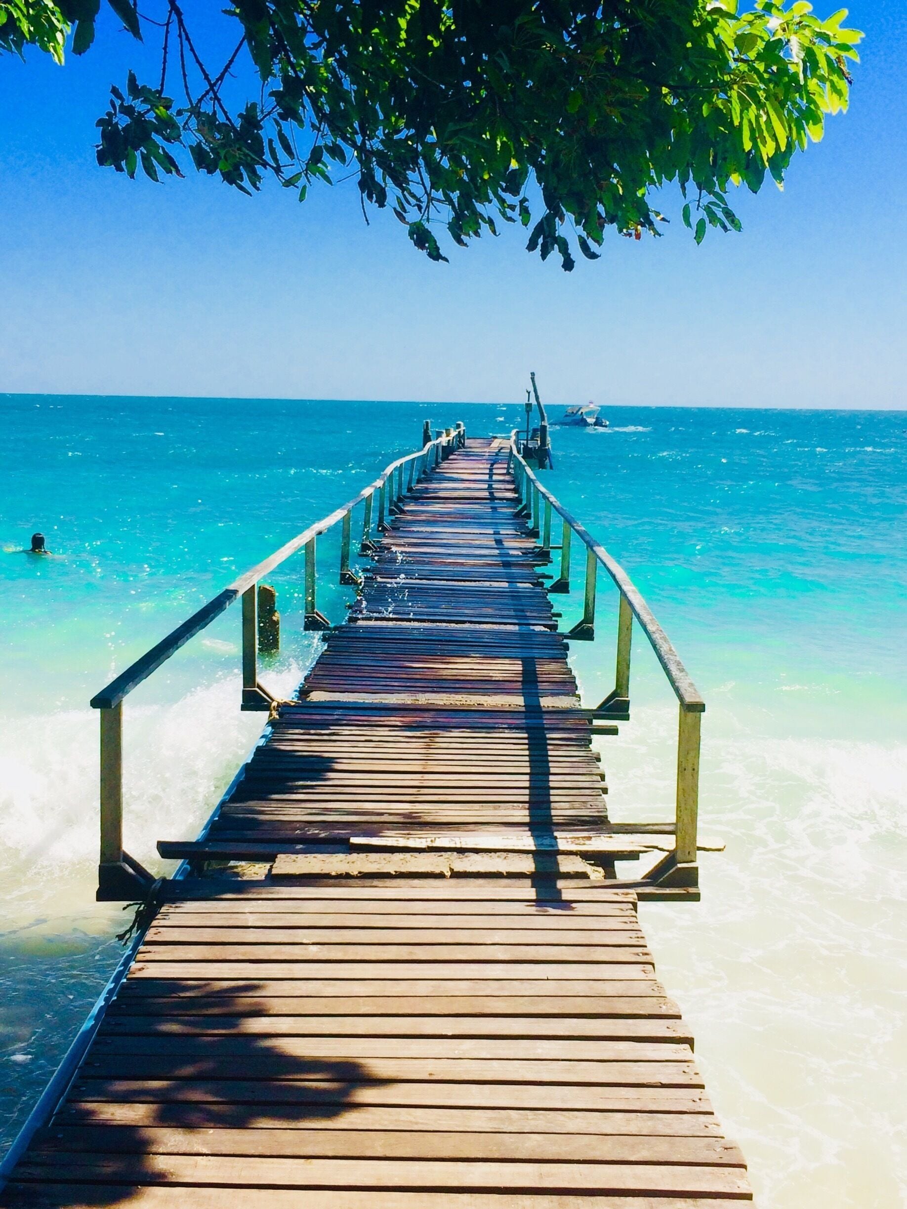 A wooden pier extending into a turquoise sea with clear skies.