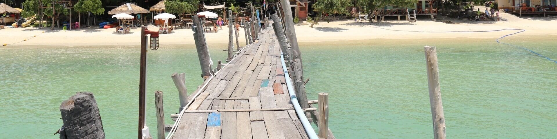 A wooden pier extending into turquoise waters, surrounded by lush greenery and beach huts.