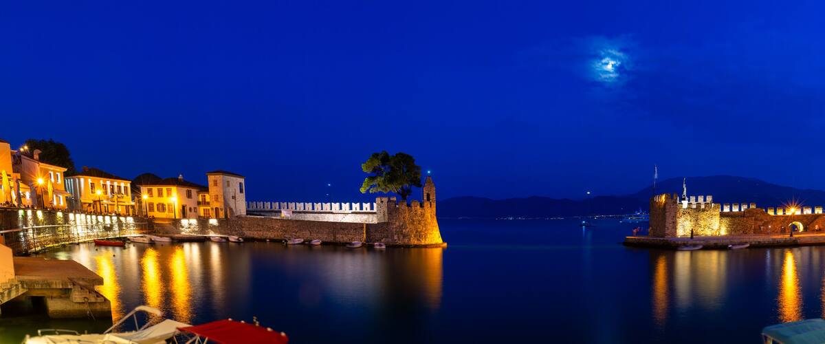 A historic waterfront with a fortified castle, calm water, and a clear night sky.