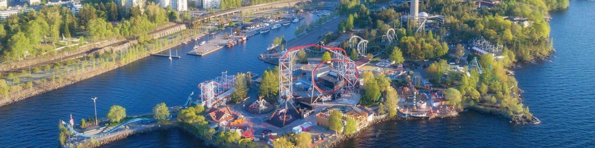An aerial view of a city with a prominent tower, a river, and a park with amusement rides.