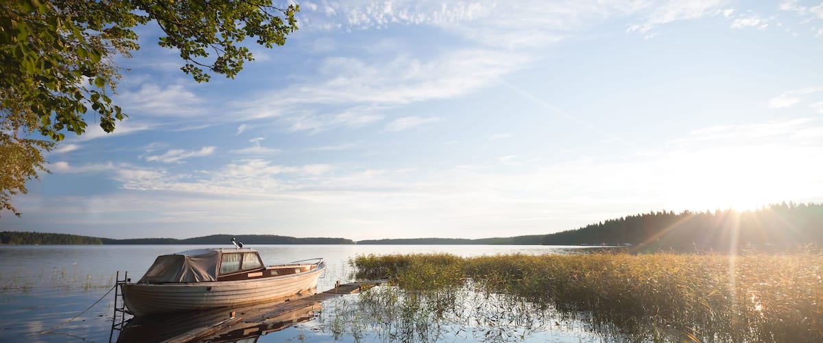A wooden boat docked at a pier extending into calm waters, surrounded by lush greenery and a serene landscape.