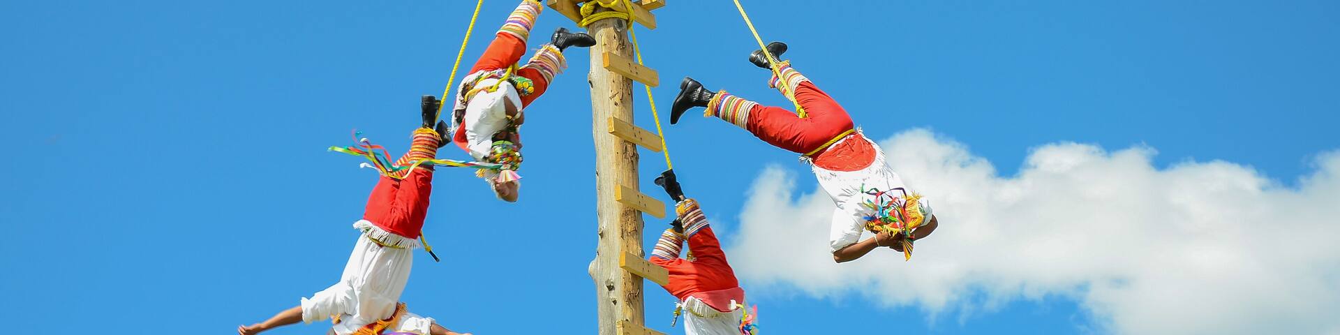 A group of people in traditional attire performing an aerial act against a clear blue sky.