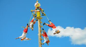 A group of people in traditional attire performing an aerial act against a clear blue sky.