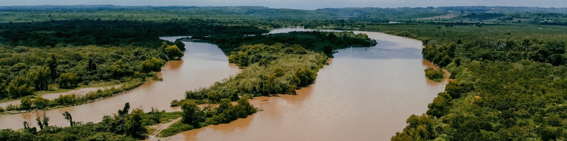 A river winding through a dense green landscape with a cloudy sky.