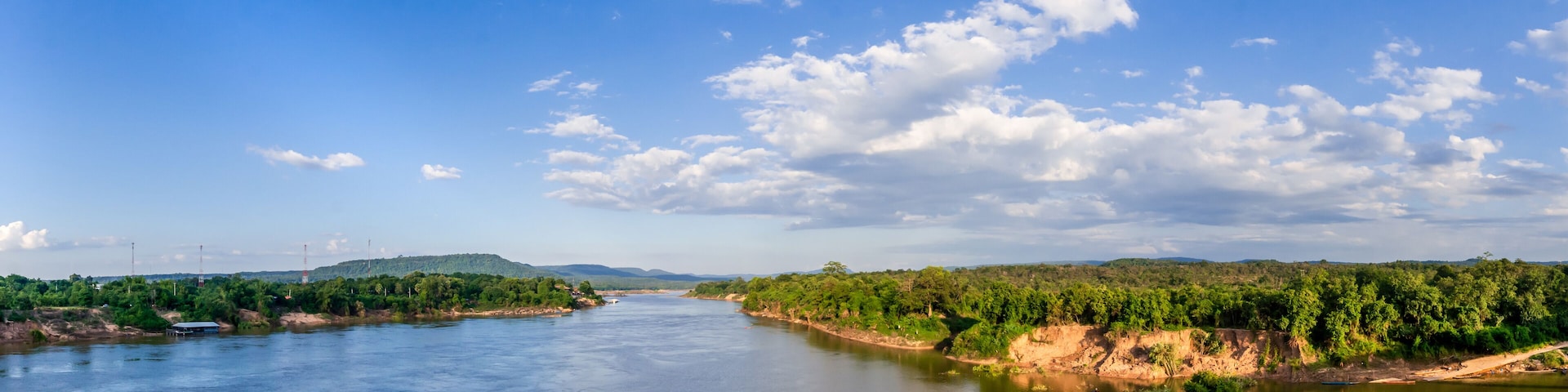 A river flanked by green hills and a clear blue sky.