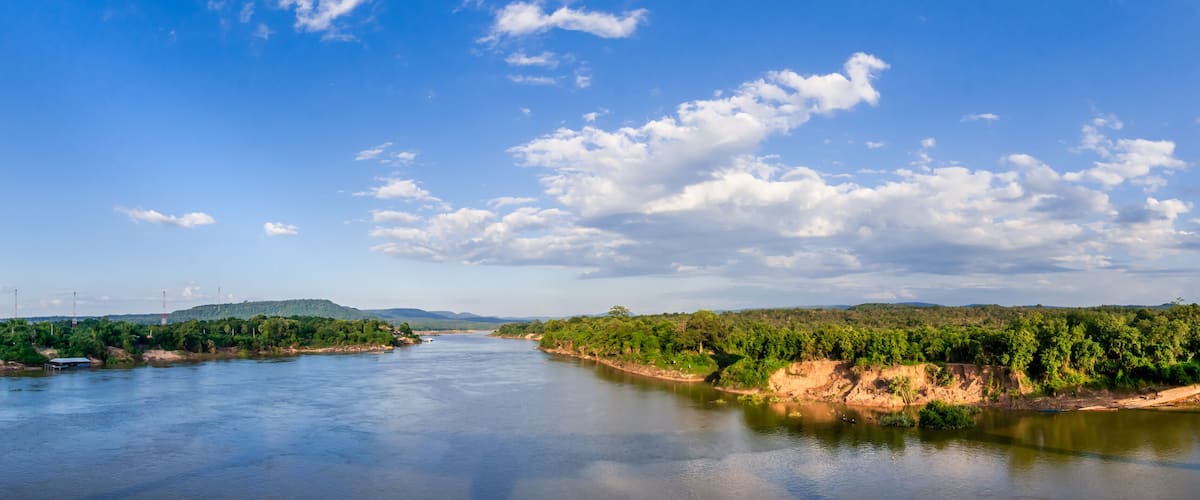A river flanked by green hills and a clear blue sky.
