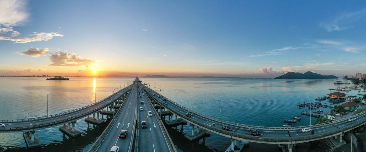 A bridge over water with vehicles, a sunset, and distant buildings.