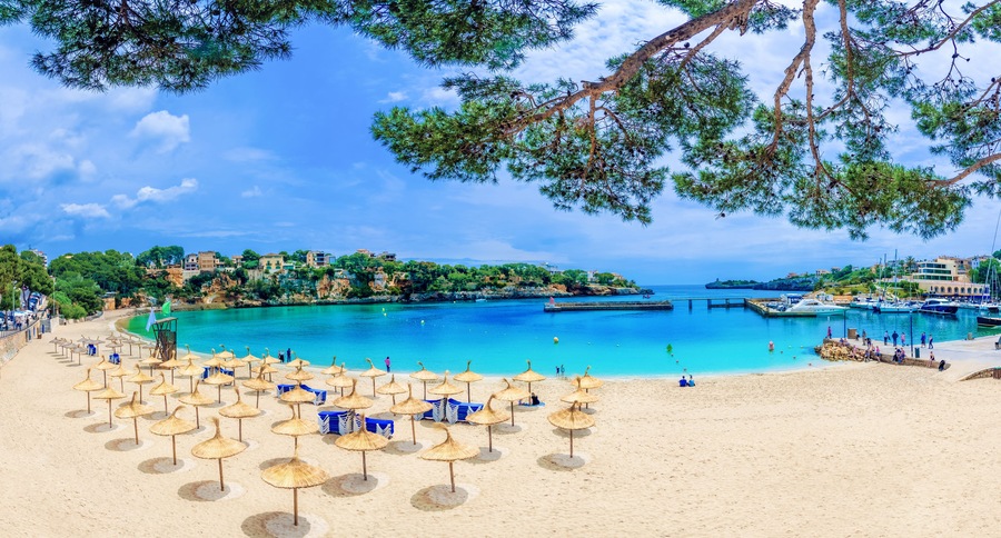 A beach with umbrellas, clear blue water, and boats.