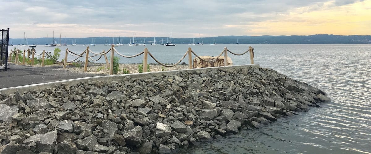 A rocky breakwater with sailboats in the background.
