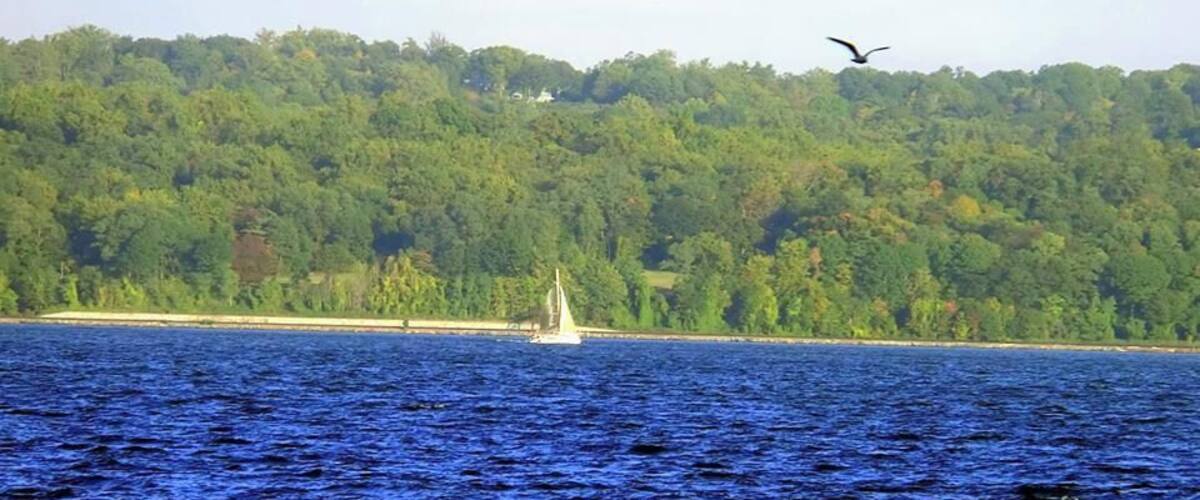 A sailboat on a body of water with a forested hill in the background.