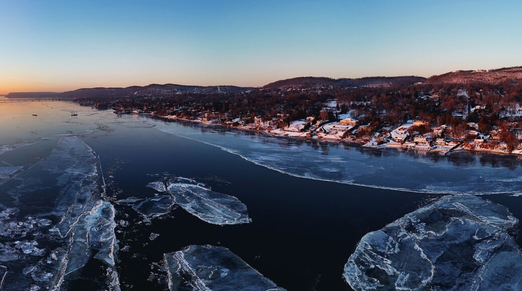 Aerial view of a frozen river reflecting the vibrant sunset, with ice sheets and distant bridge contrasting against the shoreline, Nyack, New York, United States.