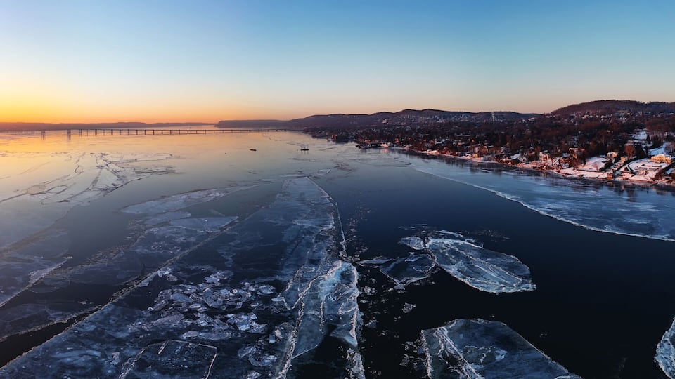 A frozen river with ice formations, a sunset, and a bridge in the background.