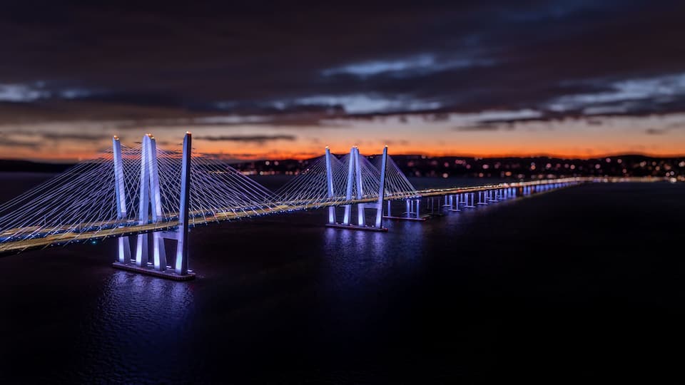 A long suspension bridge at night with illuminated cables and towers.