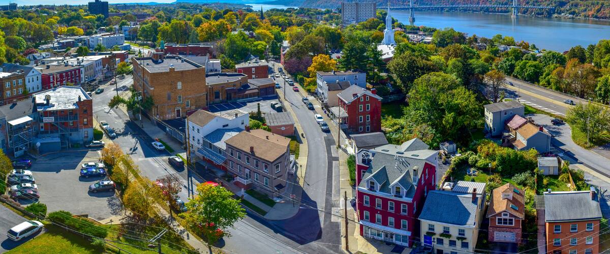 An aerial view of a town with a river, a bridge, and autumn-colored trees.