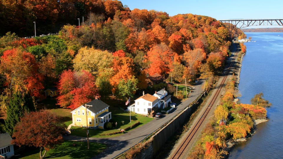 A coastal town with autumn foliage, a railway track, and a bridge in the background.