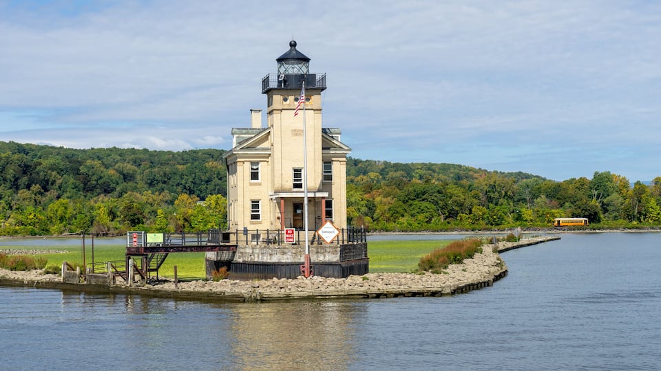 A lighthouse on a small island in a lake, surrounded by lush greenery and a clear sky.