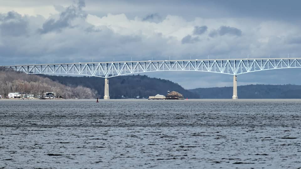 A bridge over a body of water with a forested hill in the background.