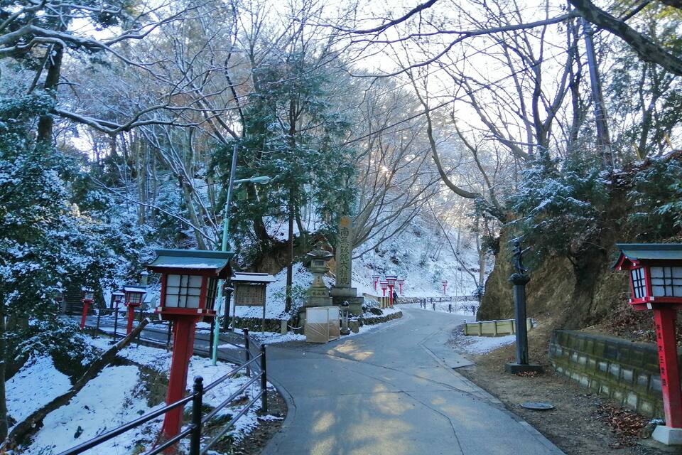 A snow-covered pathway in a park with traditional red lanterns and stone lanterns.