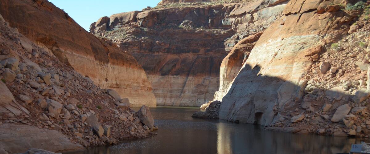 A canyon with a calm river, rocky cliffs, and a paddleboard.