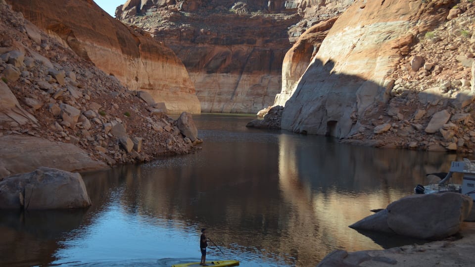 A canyon with a calm river, rocky cliffs, and a paddleboard.