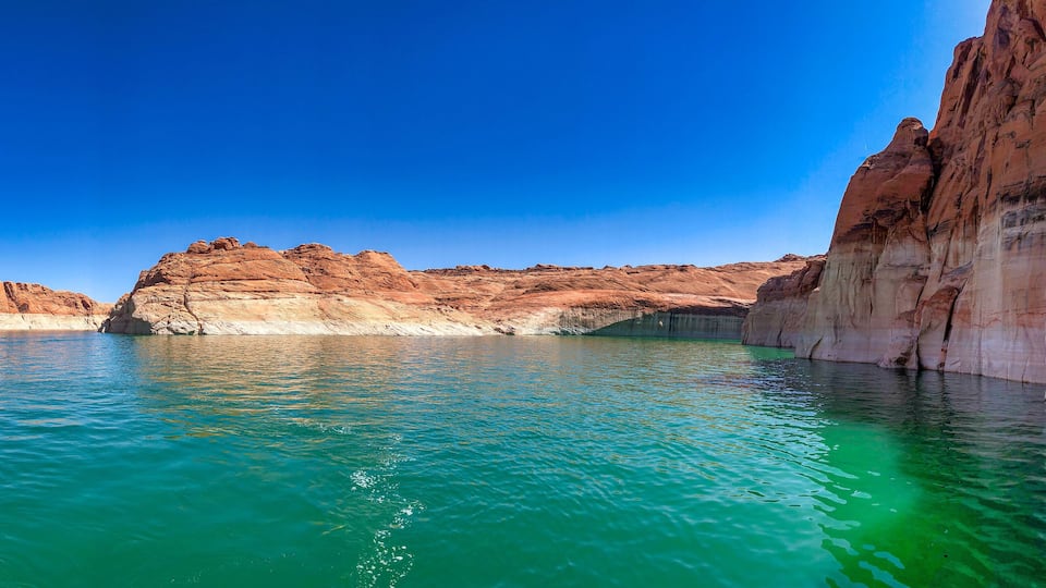 A clear blue sky, a turquoise lake, and red rock formations.