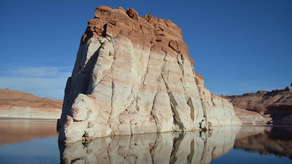 A large rock formation with a clear reflection in calm water.