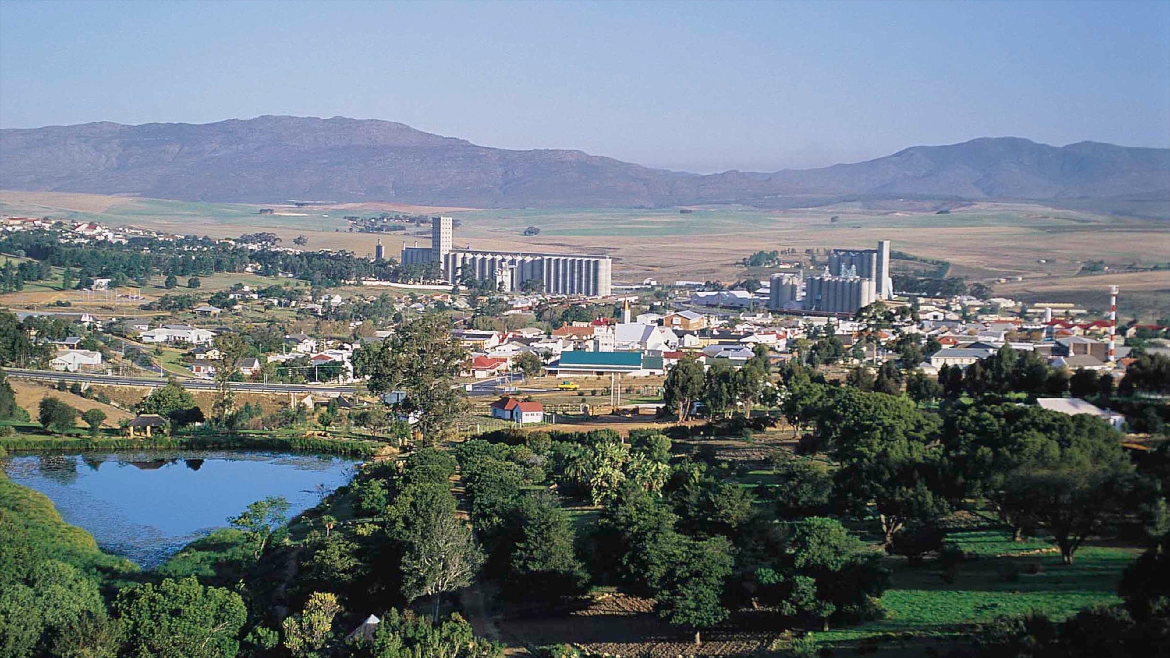 A town with industrial buildings, a river, and surrounding hills.