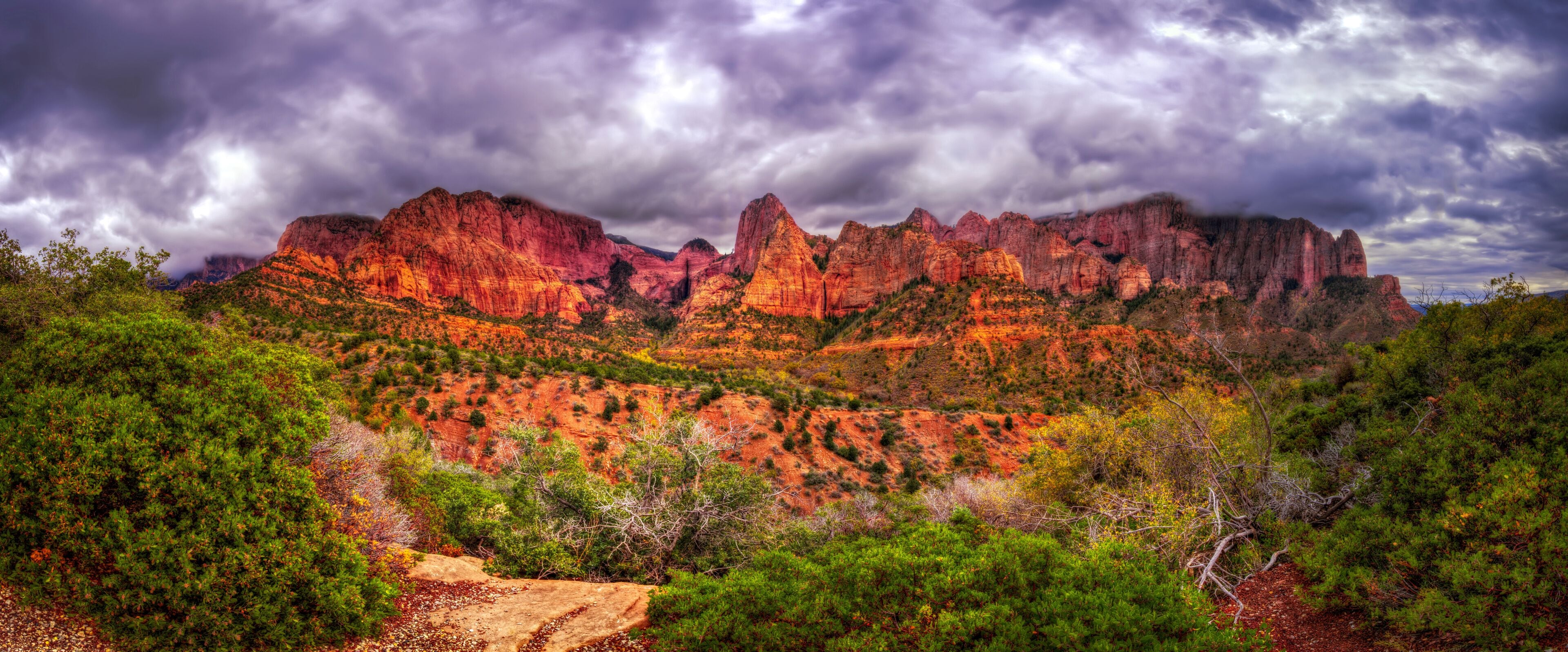 A rugged mountain range with red rock formations and green vegetation.