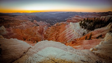 A panoramic view of a canyon with layered rock formations and a sunset in the background.