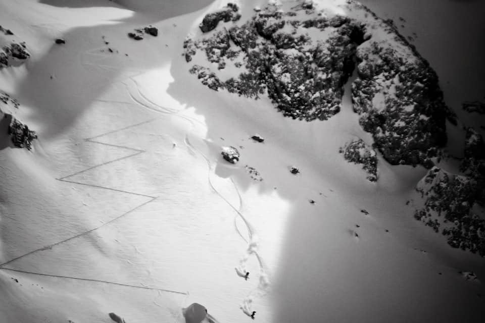 A snow-covered mountain with a ski trail and rocky outcrops.