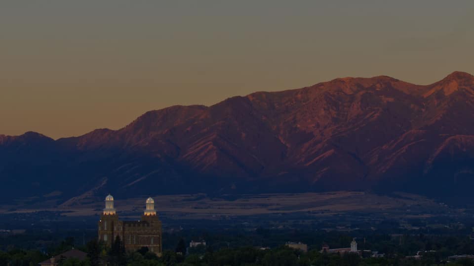 A mountain range with a church and a tower in the foreground, under a clear sky with a visible moon.
