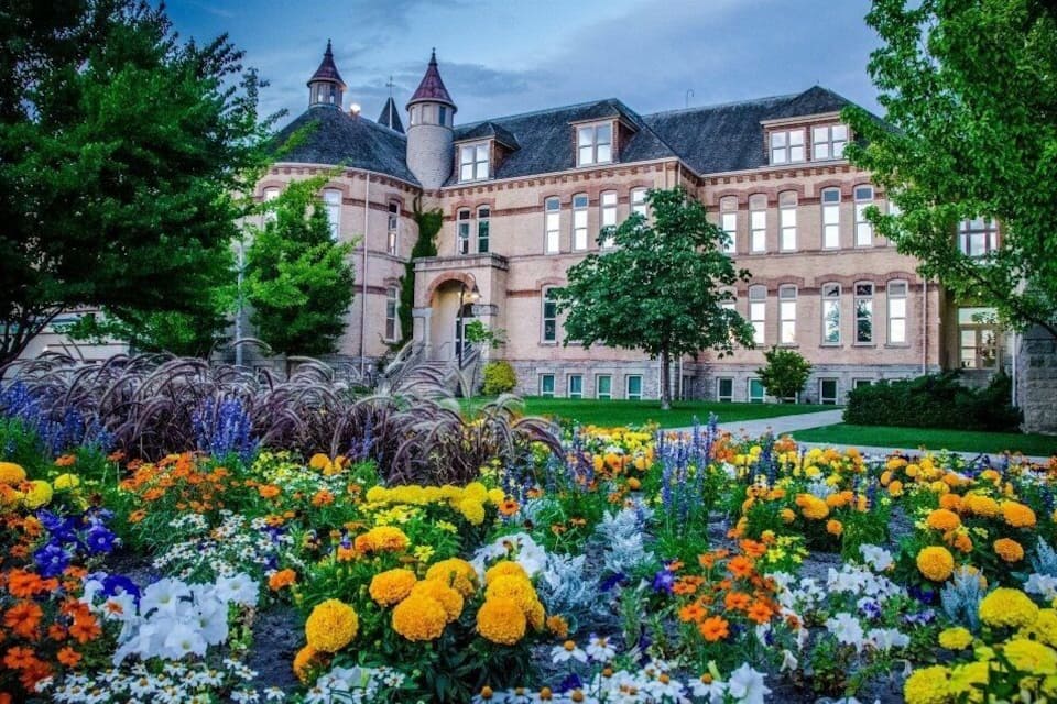 En historisk byggnad med ett torn och en trädgård med färgstarka blommor.