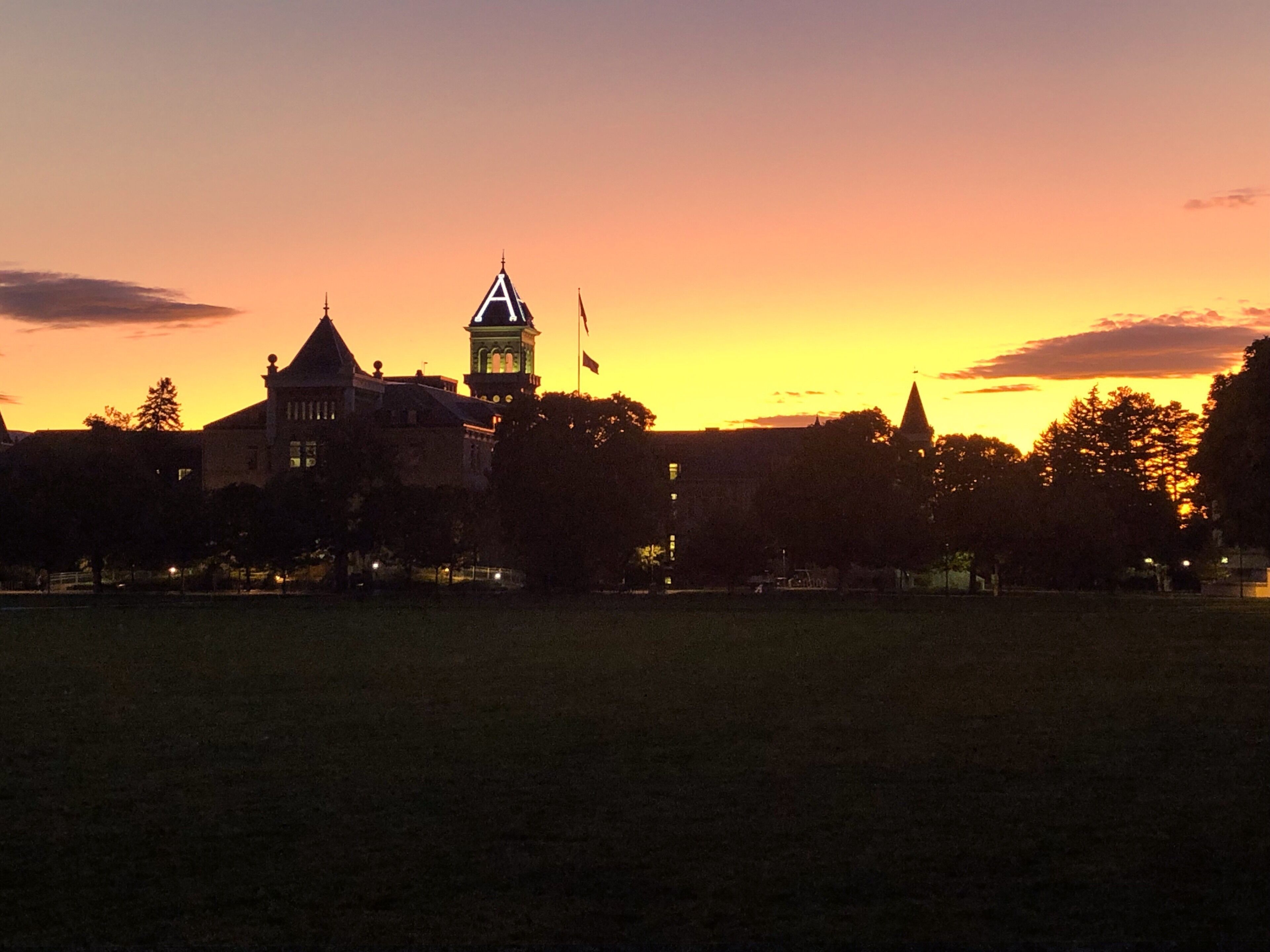 A large building with a clock tower and a flag, set against a sunset sky.