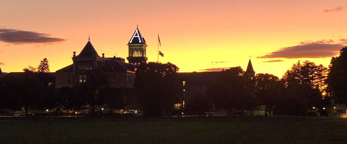 A large building with a clock tower and a flag, set against a sunset sky.