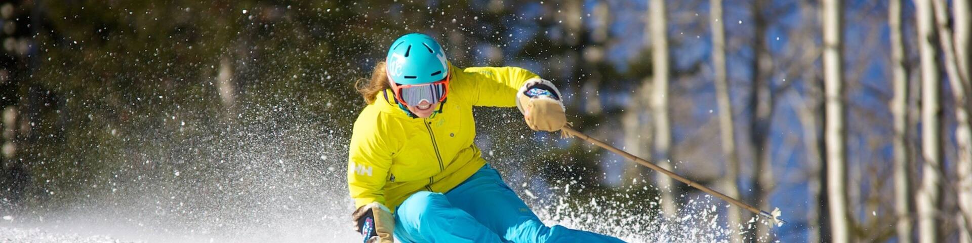 A skier in a yellow jacket and blue pants skiing down a snowy slope.