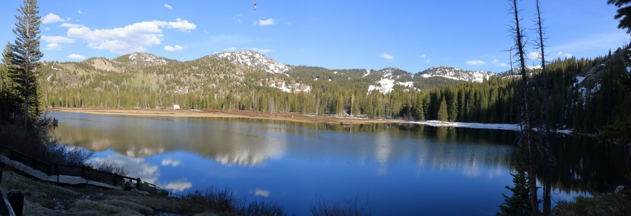 A calm lake surrounded by dense forests and snow-capped mountains under a clear sky.