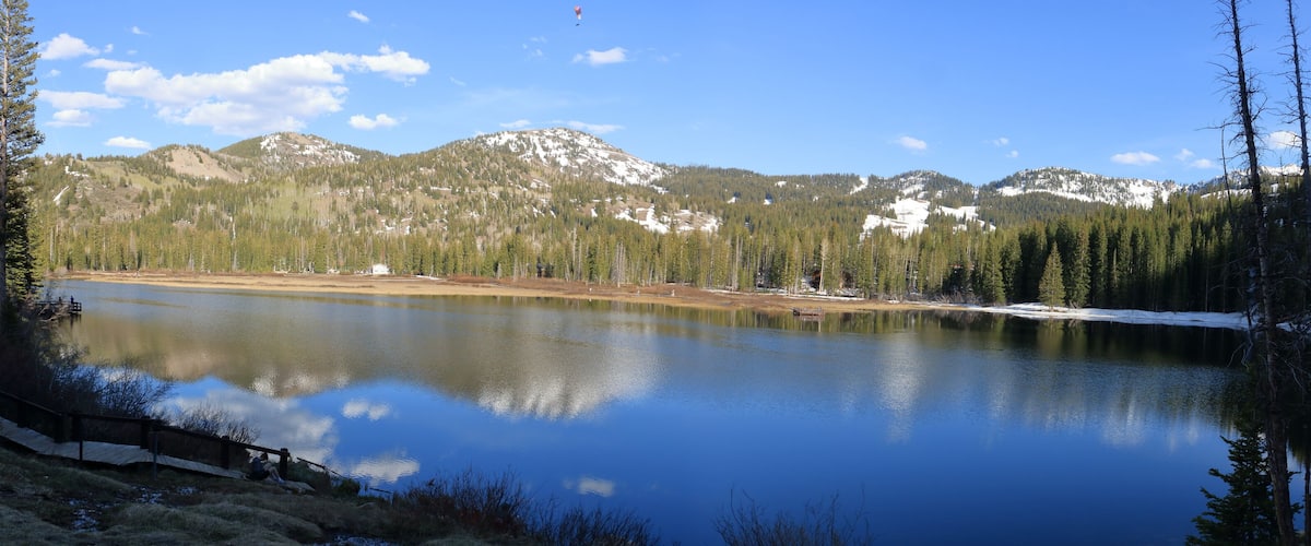 A calm lake surrounded by dense forests and snow-capped mountains under a clear sky.