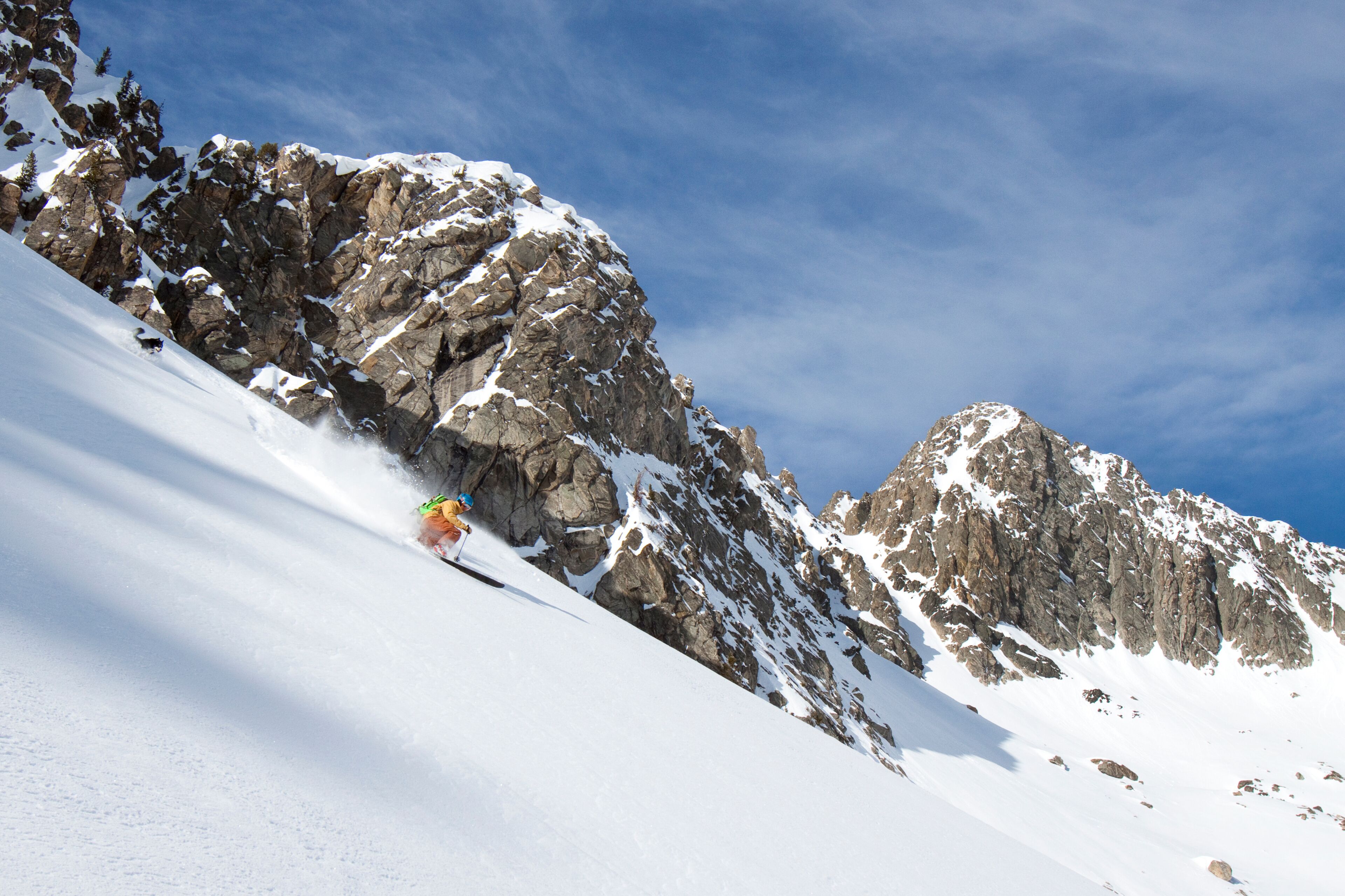 A male backcountry skier with a backpack on makes a powder turn as his dogs follows him in the Beehive Basin near Big Sky, Montana.