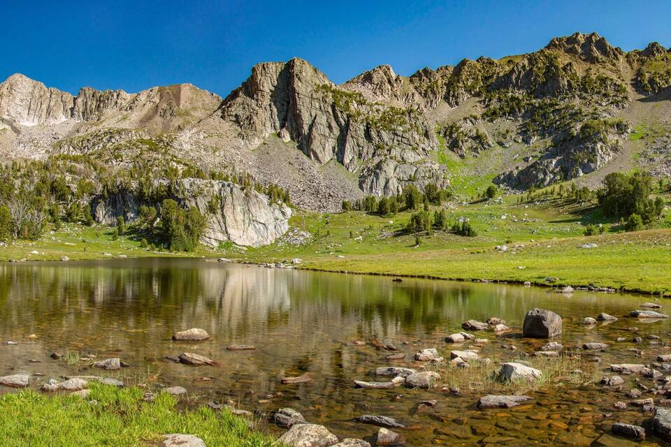 Un paisaje montañoso con un lago transparente rodeado de terreno rocoso y vegetación escasa.