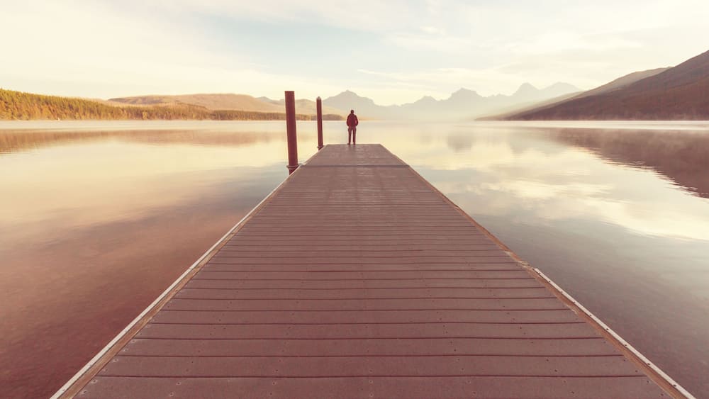 A wooden pier extending into calm waters with mountains in the background.